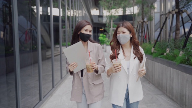 两位亚洲商务女性戴着医用口罩，拿着笔记本电脑去上班视频素材