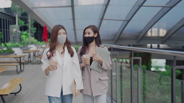 两位亚洲商务女性戴着医用口罩，拿着笔记本电脑去上班视频素材