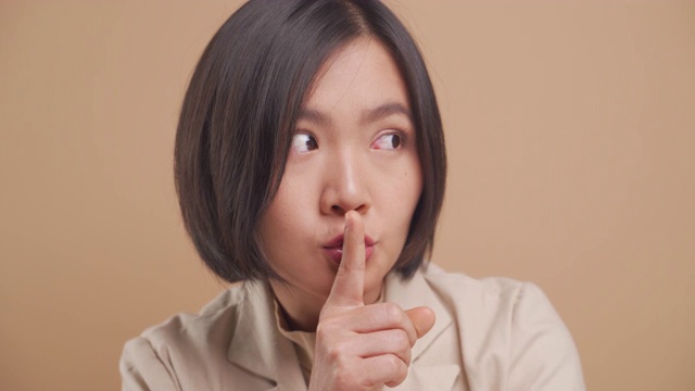 近距离拍摄的亚洲商业女性把食指放在嘴唇上意味着保持秘密孤立在米色的背景。4 k的视频视频素材