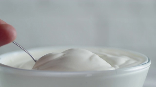 一个男人用勺子将新鲜酸奶油混合在一个碗里。视频下载