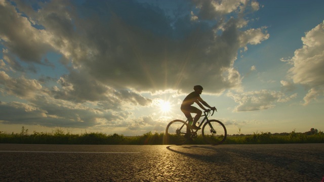 一个骑自行车的人正在高速公路上骑自行车。夕阳在背景中。镜头向后移动。4 k视频下载