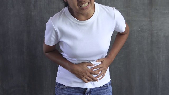 年轻的亚洲女人正遭受腹痛，女人正遭受胃痛视频素材