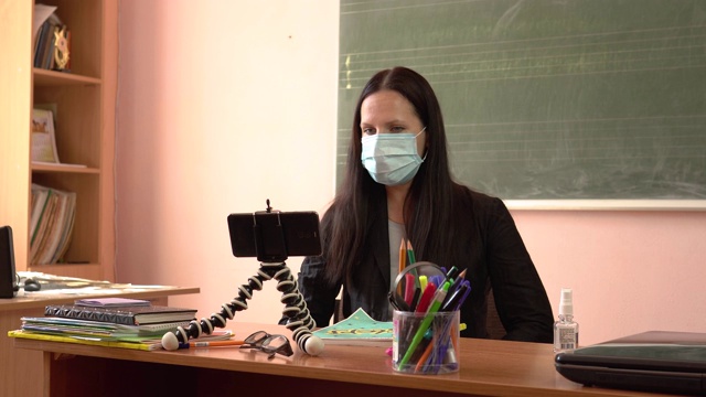 戴着防护面具的老师。隔离期间的视频教程一位年轻的老师正在上课，用智能手机拍摄自己。视频素材