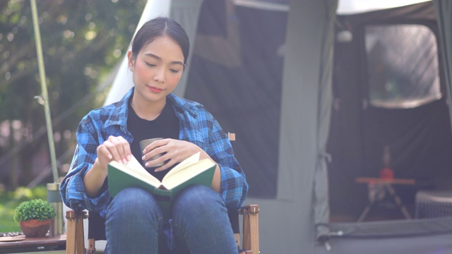 露营活动，年轻的亚洲妇女放松与热饮和阅读一本书视频素材