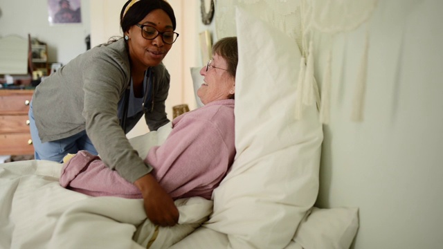 微笑的年轻护士帮助一个老女人在床上在家视频下载