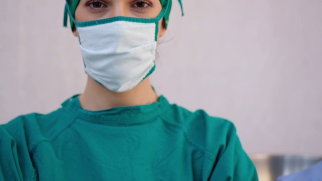 图为一名女医生或护士戴着医用帽和面罩，在医院走廊里满意地看着摄像机。医学概念，技术。视频素材