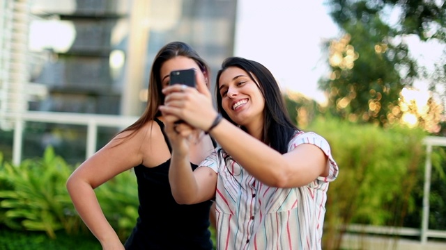 两个年轻女人在外面自拍。千禧女孩拿着智能手机拍照视频素材