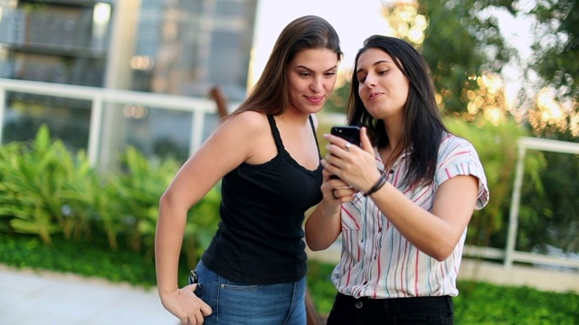 两个年轻女人在外面自拍。千禧女孩拿着智能手机拍照视频素材