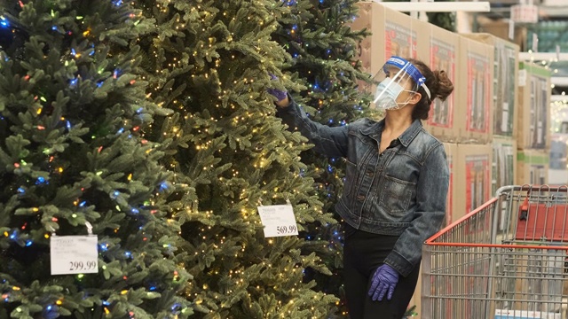 成熟的女人购买人造圣诞树戴着防护面罩，面罩和防护手套视频下载