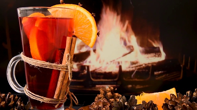 Cinemagraph -热葡萄酒杯与肉桂和橙色在桌子前燃烧的壁炉。运动的照片。视频下载