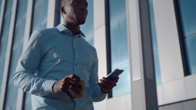 一位成功的非裔美国商人走在一间办公室附近的街道上，用智能手机查看社交网络。视频素材
