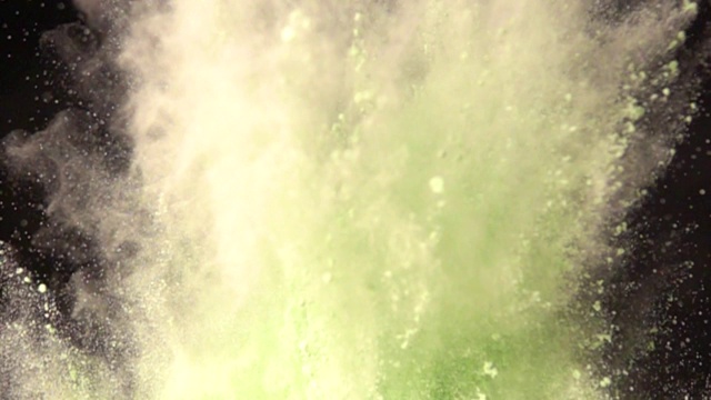超级慢镜头爆炸的彩色绿色粉末在黑暗孤立的背景。一团团的粉末向上飞，与烟混合在一起。视频下载