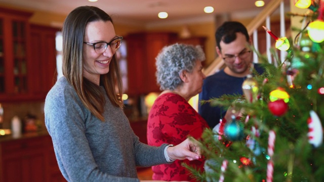 在美国一个郊区小镇的私人住宅里，两代人的大家庭在平安夜的宽敞明亮的客厅里装饰圣诞树。视频素材