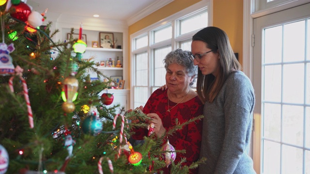 一位年长的妇女，一位母亲和她的女儿一起在客厅里装饰圣诞树。视频素材