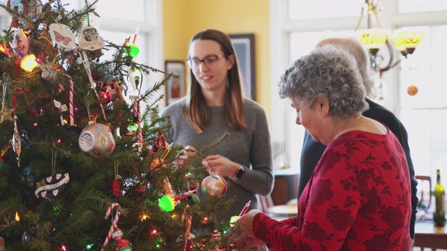 圣诞节前夕，在美国一个郊区小镇的私人住宅里，一对老人夫妇、他们的女儿和她的丈夫在宽敞明亮的客厅里装饰圣诞树。视频素材