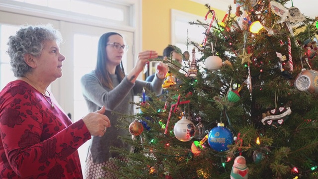 在美国一个郊区小镇的私人住宅里，两代人的大家庭在平安夜的宽敞明亮的客厅里装饰圣诞树。摄像机绕着树移动。视频素材