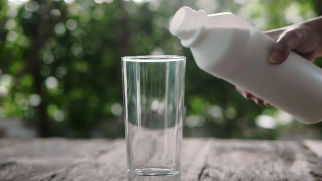 在夏日花园的慢动作中，将牛奶从一个玻璃罐子倒入一个透明的玻璃杯中视频素材