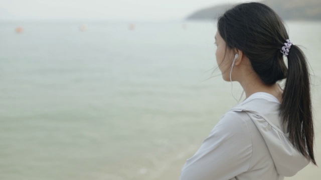 亚洲女运动员穿着运动服，听着音乐，望着大海。视频素材