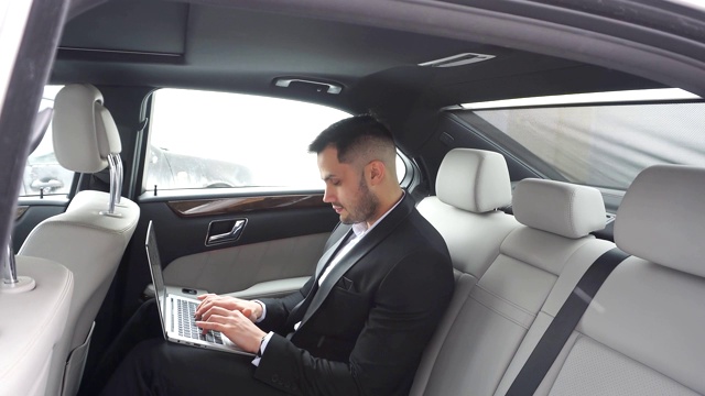 男士穿着正装，在豪华轿车里开着笔记本电脑视频素材