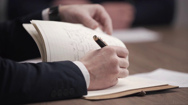 男手执笔，用笔在记事本上写清单或业务资料。手写商务报告，在公司会议室的办公桌上做书面记录。视频下载