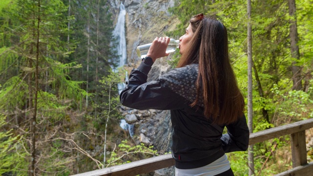 女子在瀑布边休息，用可重复使用的水瓶补水视频素材