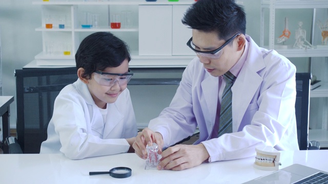 亚洲男牙医边讲边正确地给小男孩讲解刷牙，小男孩们在教室的实验室里听着。视频素材