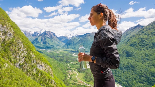 一名女子在山间徒步旅行后休息，喝着一瓶水视频素材