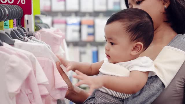 一个亚洲男婴和他的母亲抱在一个儿童服装店。视频下载