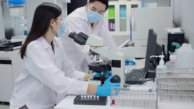 科学家正在看显微镜，男女医生在讨论。一种用电脑设备进行的血液测试。视频下载