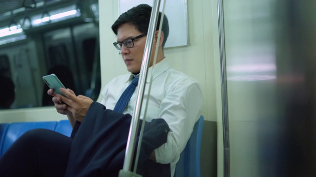 微笑的男性通勤者在地铁列车上用手机发短信视频下载
