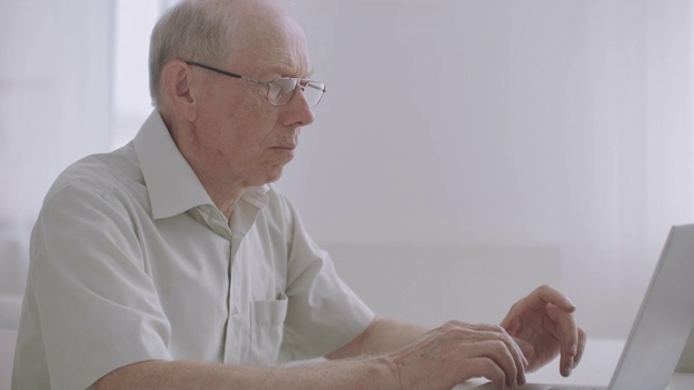 一位戴着眼镜的老人正在用笔记本工作，上网，通过短信聊天，在键盘上打字视频下载