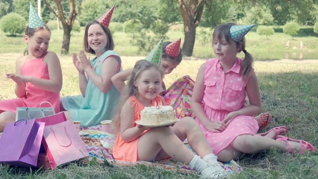 女孩们坐在公园的草地上。他手里拿着一个生日蛋糕。视频下载