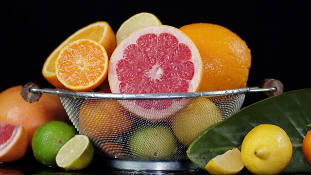 各种柑橘类水果装在滤锅里，叶子上滴着水。视频素材