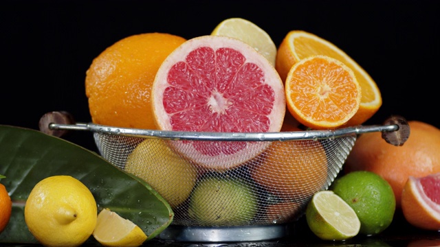 各种柑橘类水果装在滤锅里，叶子上滴着水。视频素材