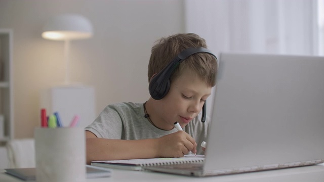 男孩在家里画画，和朋友在网上聊天，用笔记本电脑和带麦克风的耳机视频下载