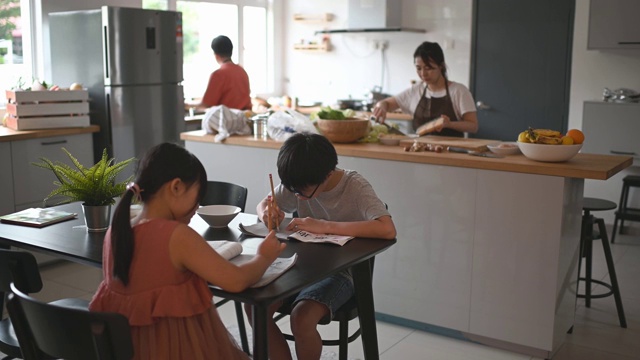 两个孩子在家学习写中国书法，而他们的母亲在厨房柜台准备食物视频素材