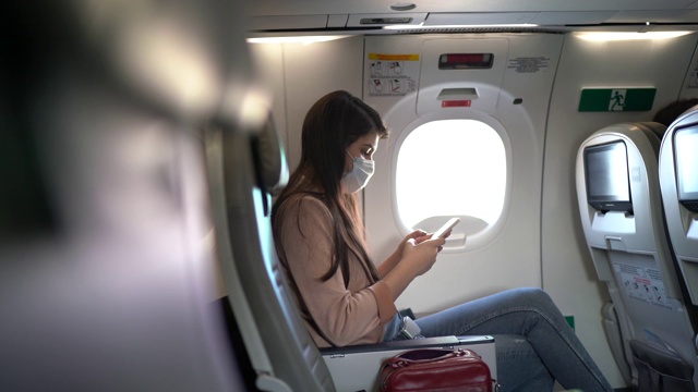 一名年轻女子戴着口罩坐在飞机座位上打电话视频素材