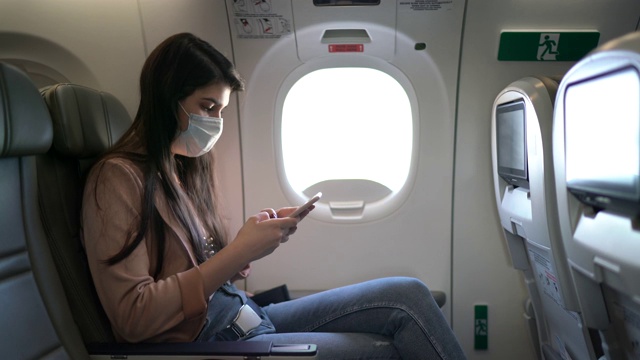 一名年轻女子戴着口罩坐在飞机座位上打电话视频素材