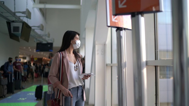 年轻的女旅行者透过窗户看，在机场使用电话-戴口罩视频素材