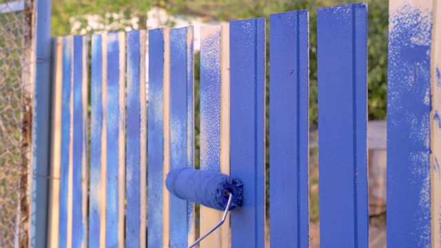在地块或建筑工地上，工人用滚轴和蓝色染料涂木栅栏板。在庭院或乡村房屋中进行建筑或修理工作视频素材