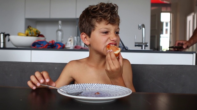 沉思的男孩在早餐桌上吃着面包和果冻视频下载