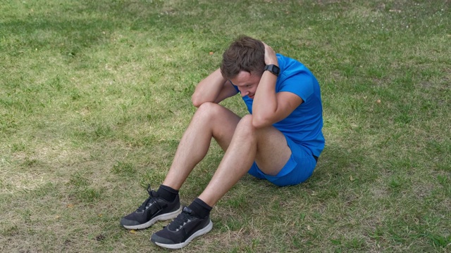 一名男子在公园的草地上锻炼腹部肌肉。视频下载