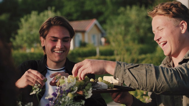 在社交聚会上，微笑的男子在切菜板上给男性朋友葡萄视频下载