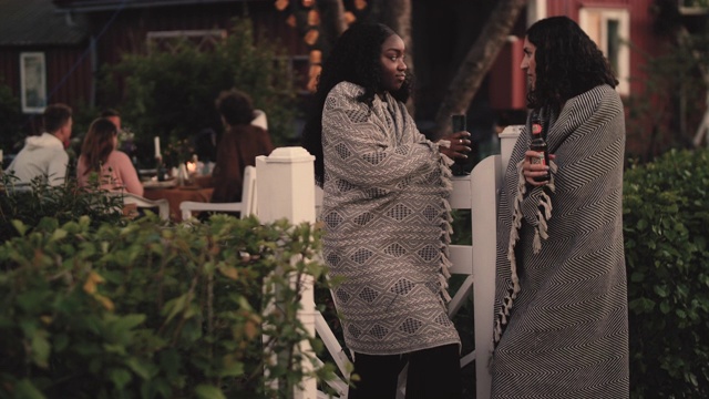 在游园会期间，女人拿着啤酒瓶站在院子旁边说话的慢动作镜头视频素材