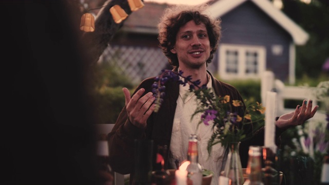 慢镜头拍摄的微笑的男子在花园聚会期间坐在院子里和朋友聊天视频素材