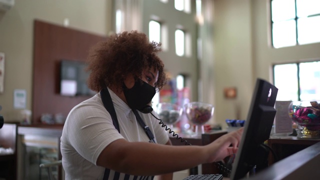 女服务员一边打电话一边在电脑上记录客户的订单，她还戴着口罩视频下载