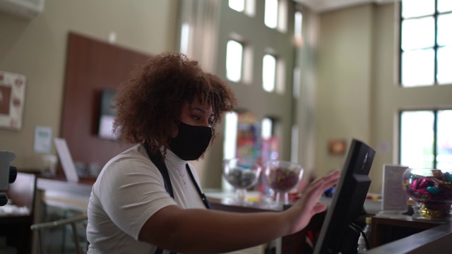 在咖啡店里，女服务员戴着口罩在电脑上登记顾客的订单视频素材