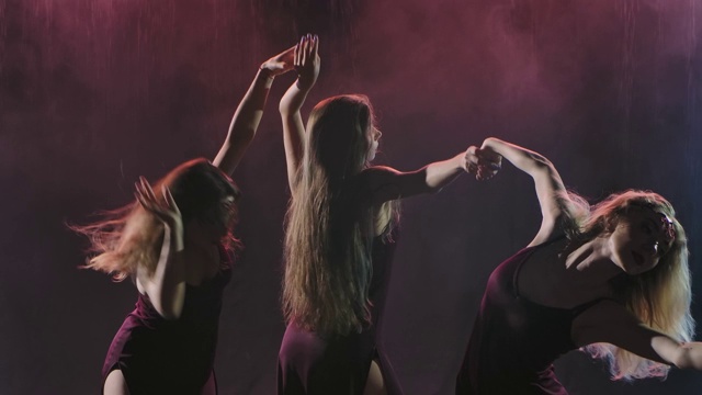 一群穿着长裙的女子在烟雾缭绕的背光演播室里跳着现代舞蹈。缓慢的运动。近距离视频下载