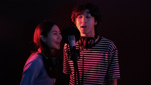 年轻的亚洲有吸引力的音乐家一起在现代录音棚录制新歌快乐歌唱。两个年轻人一起工作的新音乐专辑在工作室的黑暗背景。视频下载