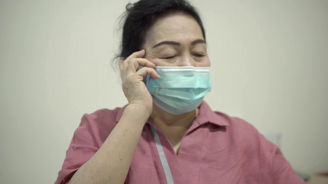 一位年长的亚洲女性戴着防护面具打电话。视频素材
